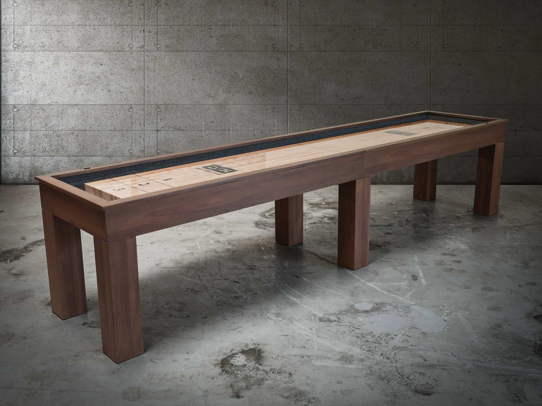 12-foot Paula Parsons Shuffleboard Table by Doc & Holliday in Grey Walnut, angled lifestyle view on concrete floor capturing modern lines, rich maple playfield, and bold Parsons design.