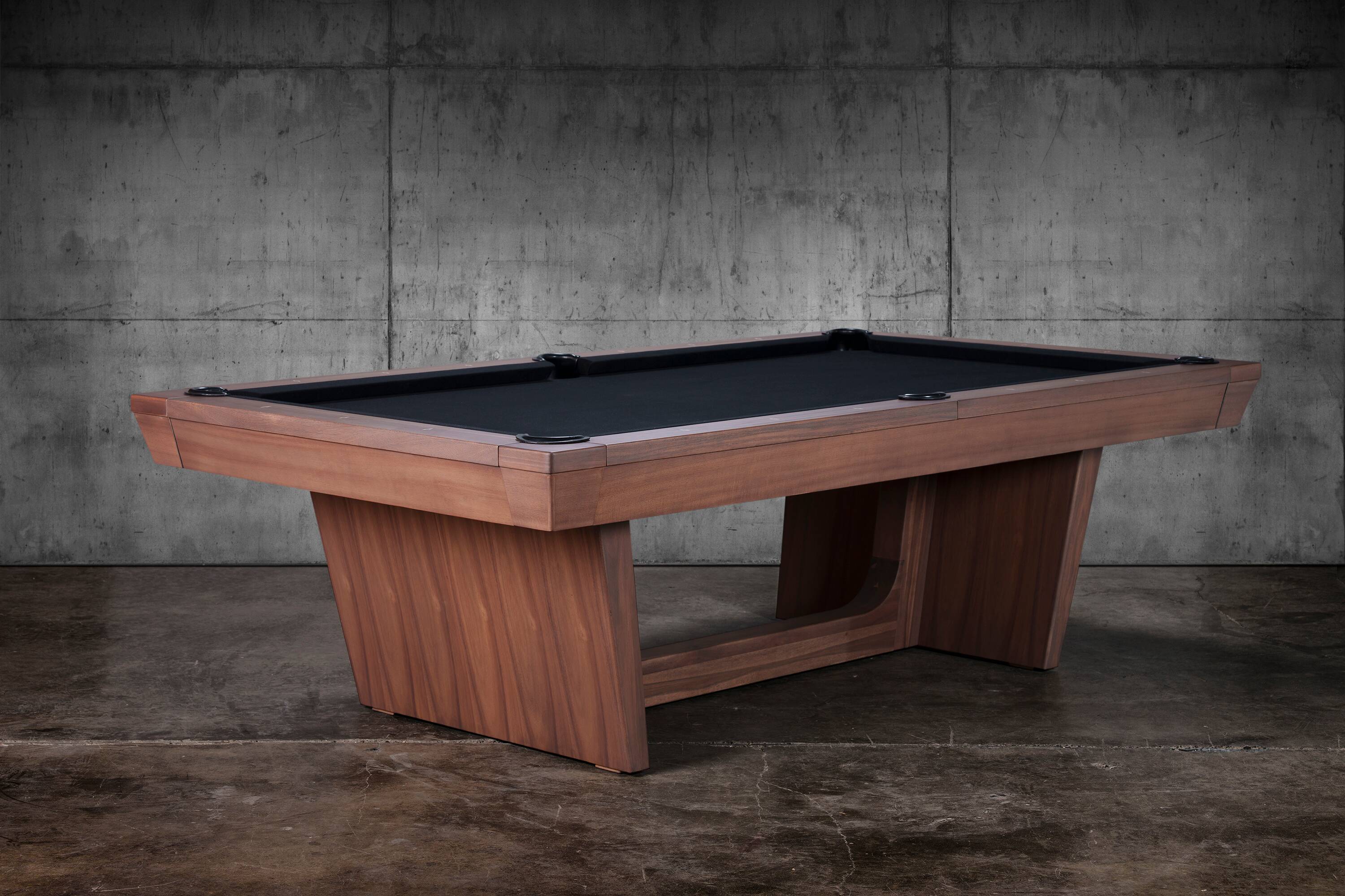 Three-quarter hero from the photo shoot of the Kaci slate pool table by Doc & Holliday Billiards in Grey Walnut. Sleek tapered pedestal legs and a lean tapered rail-and-apron profile give it a confident, contemporary stance, with the Grey Walnut grain warming the frame under studio light. A design-forward slate billiard table that carries the American spirit of Doc & Holliday into modern lounges and real homes.