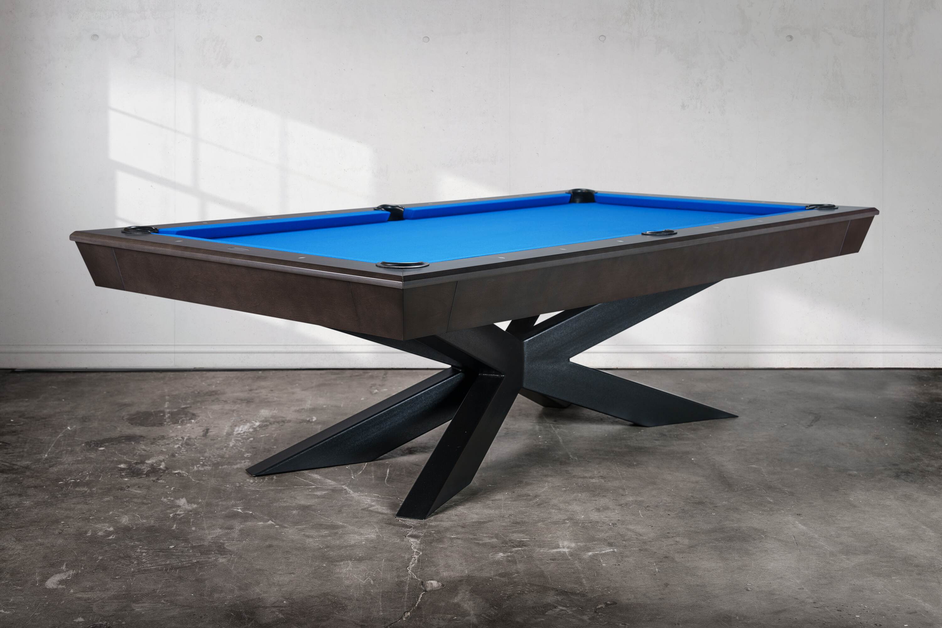 Three-quarter view of the Jett Stealth Edition pool table, showing its anchored steel base and Smokehouse maple finish. A USA-built centerpiece for modern luxury interiors and designer projects.”