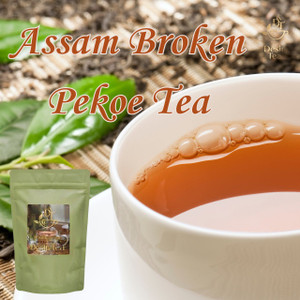 A close-up view shows a white cup filled with frothy brown Assam tea, with fresh green leaves in the blurred background.