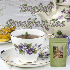 A floral porcelain teacup and matching teapot decorated with purple violets sit beside a small plate of decorated cookies.