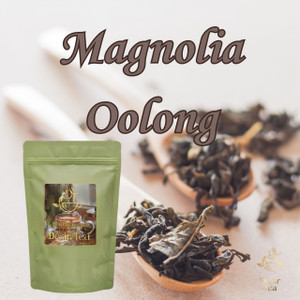 Artisanal loose dark tea leaves scooped beside a green pouch of Desir Tea on a warm wooden tabletop.