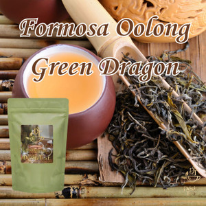 Traditional dark oolong leaves resting inside a shallow clay dish next to a branded green tea pouch on a wooden board.