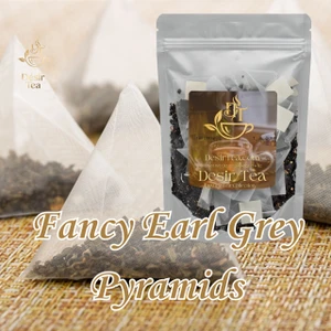 Black tea pyramid bags displayed beside a classic ceramic cup of dark brew garnished with a fresh slice of lemon.