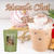 A clear plastic cup holds iced masala chai topped with whipped cream and spice, alongside holiday ornaments on a white surface.