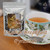 A rich brew in a ceramic teacup accompanied by pyramid sachets and loose leaves scattered across a rustic wooden tabletop.