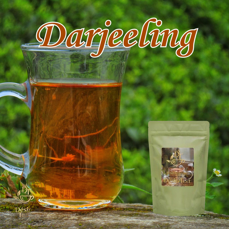A clear glass pitcher filled with warm amber Darjeeling tea rests on a rustic wooden surface against a lush green outdoor background.