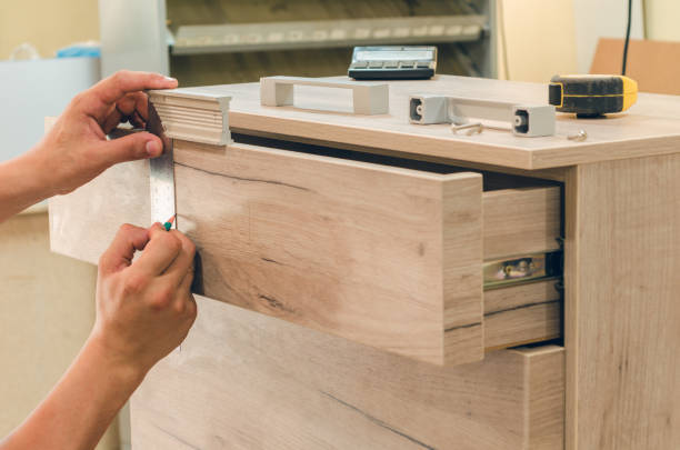Worker measuring wooden drawer front while assembling new office storage cabinet.