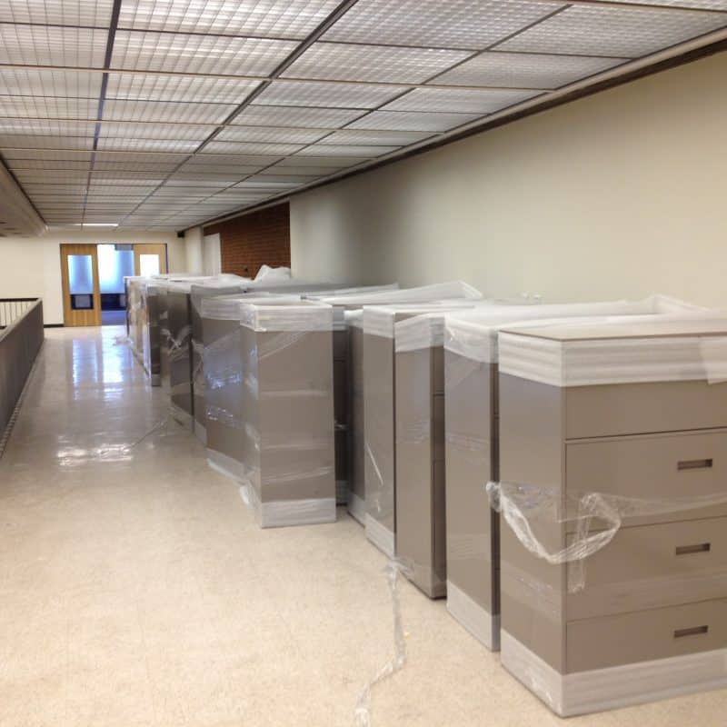 Row of wrapped filing cabinets lined up in hallway ready for office furniture installation.