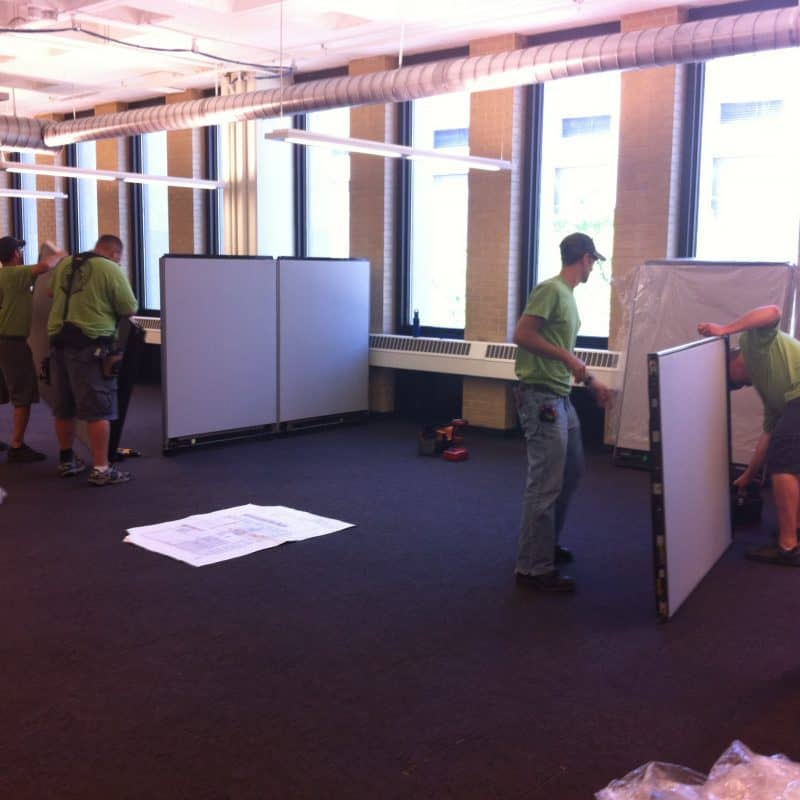 Office installation crew in green shirts assembling office cubicle panels in open office.