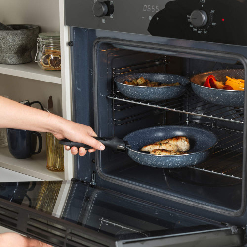 Hand placing a detachable-handle frying pan with cooked chicken into an oven