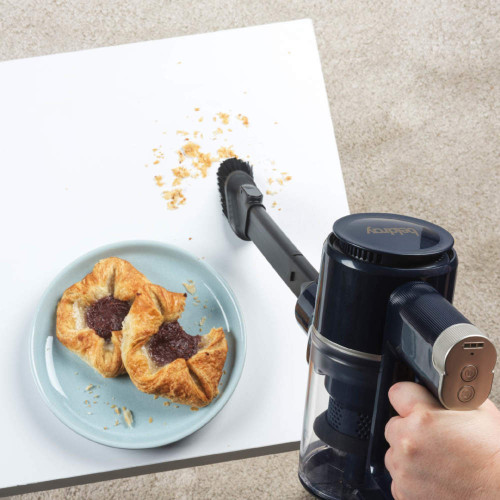Handheld vacuum cleaning pastry crumbs from tabletop next to plate with pastries