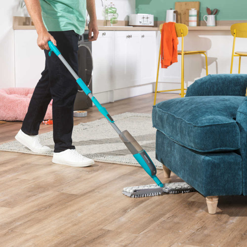 Spray mop cleaning under blue sofa on wooden floor in modern kitchen living space