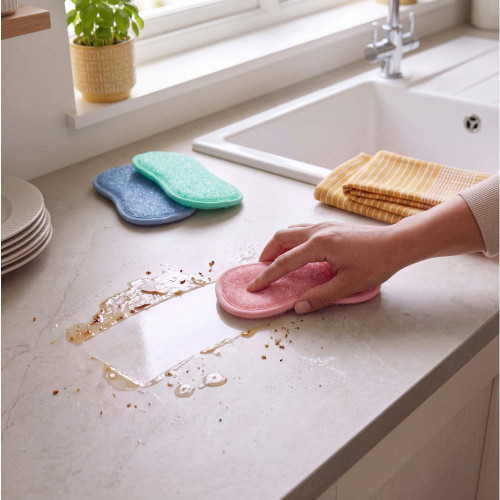 Hand using pink sponge cloth to wipe kitchen worktop by sink