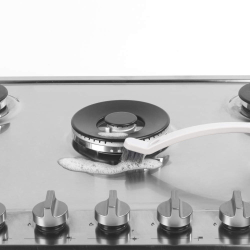 Cleaning a stainless steel gas hob with a brush and soapy water. Suitable for kitchen appliance listings.