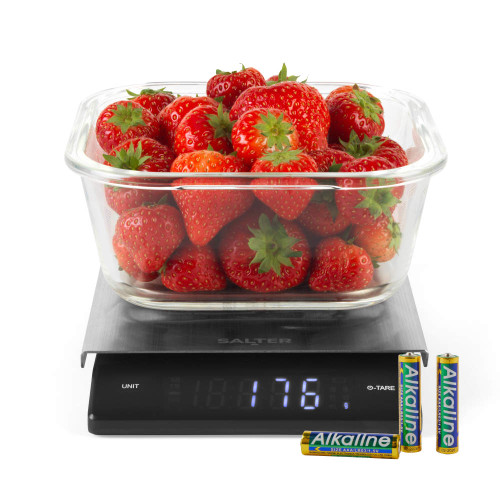 Glass bowl of strawberries on digital kitchen scale, LCD showing 176g, with AA batteries