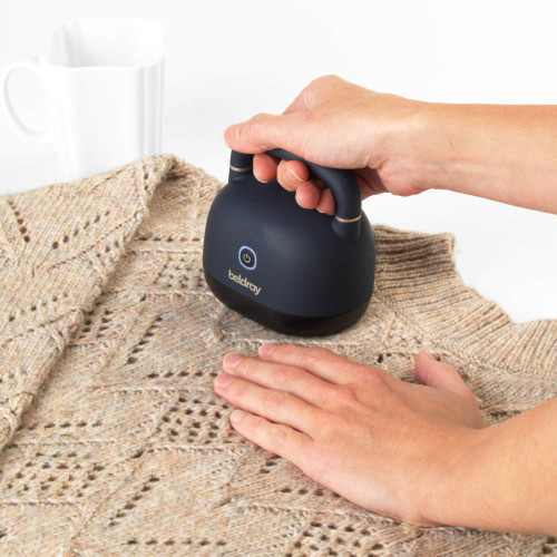 Handheld electric fabric shaver being used on knitted jumper
