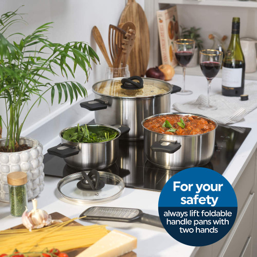 Set of three stainless steel saucepans with foldable handles on hob, food inside.