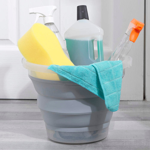 Grey cleaning bucket with spray bottles, yellow sponge and blue cloth on floor.