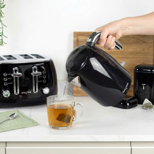 Black electric kettle pouring hot water into tea mug on kitchen counter