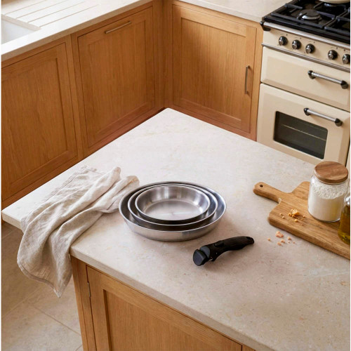 Set of three stainless steel frying pans with black removable handle on kitchen worktop