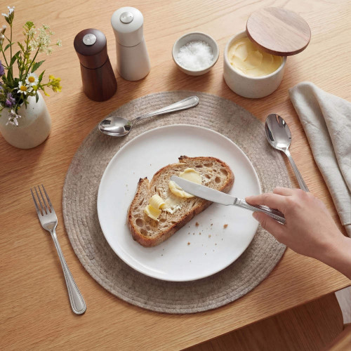 Hand spreading butter on slice of bread with silver cutlery on breakfast table.