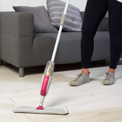 Pink spray mop in use on light wood floor, next to grey sofa.