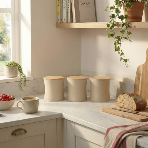 Set of three beige kitchen storage jars with wooden lids on marble worktop