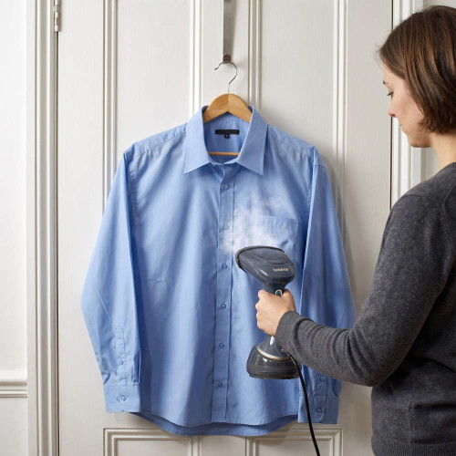 Handheld garment steamer used on light blue shirt hung on white door