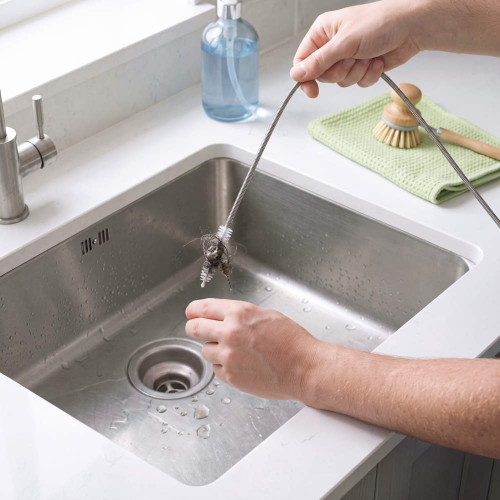 Flexible silver drain snake removing hair clog from kitchen sink