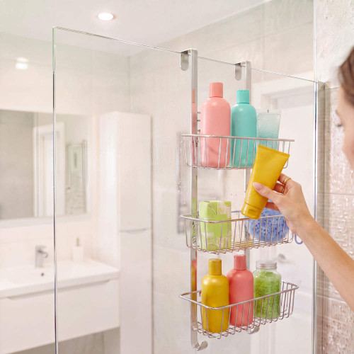 Chrome over-shower caddy with three baskets hanging on a glass shower screen