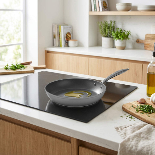 Grey non-stick frying pan with oil on induction hob in modern kitchen