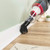 Vacuum cleaner with brush attachment cleaning dust from skirting board on wooden floor