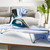 Teal and silver steam iron on ironing board with blue shirt, sofa and laundry in background