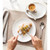 Person cutting pistachio croissant on white plate with coffee, for breakfast tableware listing