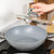 Grey non-stick wok with glass lid shown on a kitchen hob
