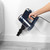 Corded handheld vacuum cleaner in navy, cleaning skirting board near grey sofa.