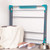 Folding grey and teal clothes airer leaning against wall, with basket, blanket and shoes