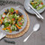 Contemporary table setting with mixed salad in grey bowl and silver cutlery.