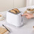 White 2-slice toaster with textured finish, in use, shown toasting seeded bread