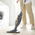 Person using a black and gold steam mop to clean a cream rug in a bright laundry room