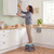 Woman standing on grey folding step stool to reach kitchen cupboard