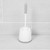 White toilet brush with grey handle in matching holder on bathroom tiles