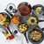 Set of non-stick grey saucepans and frying pans with assorted cooked food, viewed from above