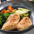 Two cooked chicken breasts with carrots, broccoli, and leeks in a non-stick frying pan