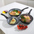 Set of three black non-stick frying pans with cooked fish, chicken, and vegetables.