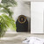 Black and gold mechanical bathroom scale on tiled floor next to towel and plant.