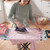 Steam iron in use on pink cotton shirt, indoor laundry setting, for garment care.