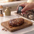 Digital meat thermometer measuring temperature in cooked steak on wooden board