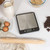 Black digital kitchen scale with stainless steel platform, shown for baking with ingredients.
